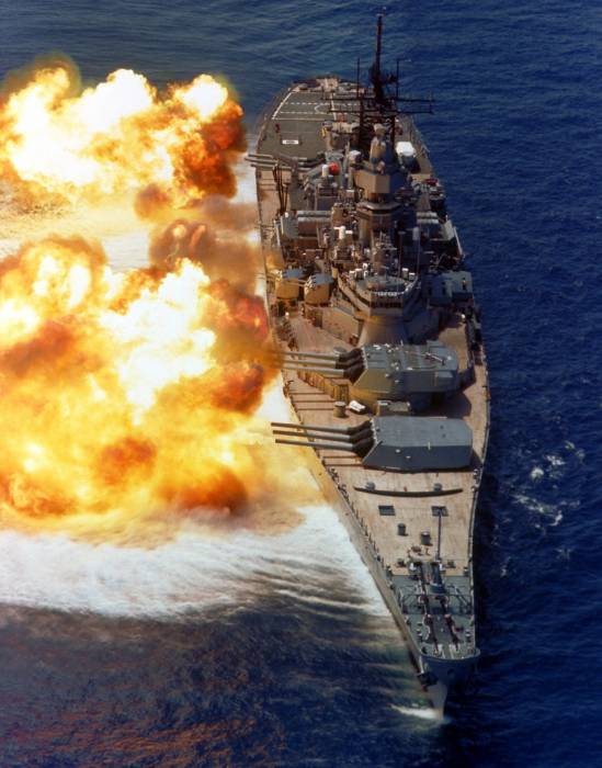 A bow view of the battleship USS IOWA (BB-61) firing its Mark 7
16-inch/50-caliber guns off the starboard side during a fire power...